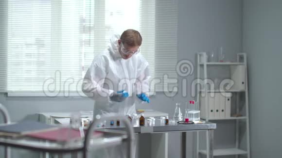 戴防护工作服眼镜和医用手套的人看实验室的设备视频的预览图