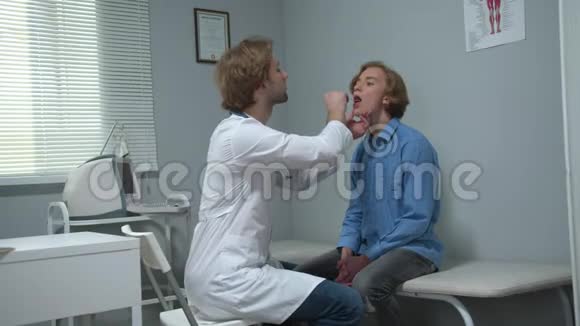 男孩坐在医院的柜子里医生用棍子检查他的嘴视频的预览图
