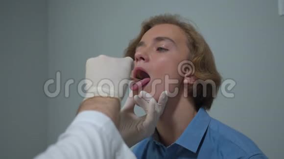 男孩坐在医院的柜子里医生用棍子检查他的喉咙视频的预览图