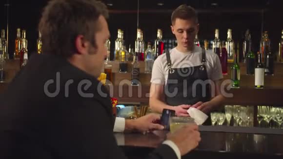 男人坐在酒吧拿着信用卡和酒保说话视频的预览图