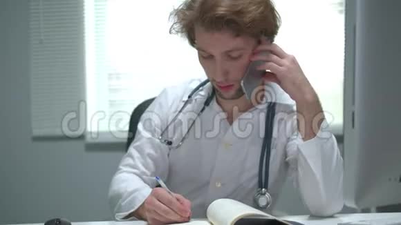 医生坐在医院的一张桌子旁打电话写信视频的预览图