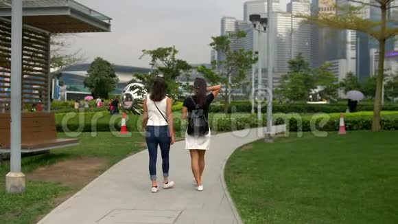 两个年轻的女人带着绿草和4k左右的建筑物在公园里散步视频的预览图
