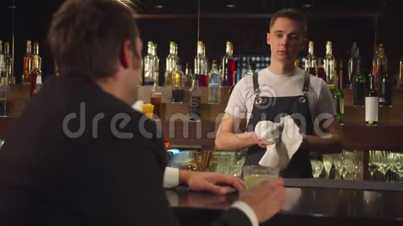 男人喝酒和擦玻璃的酒保说话视频的预览图