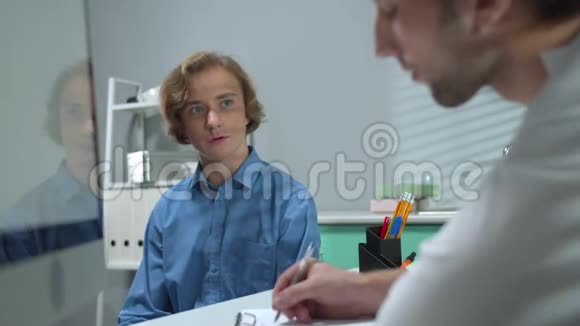 男孩坐在医院的柜子里和写信的医生交谈视频的预览图