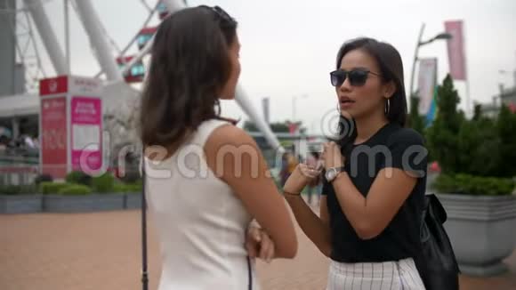 阴天4k两个美丽的亚洲女人在大摩天轮边聊天视频的预览图