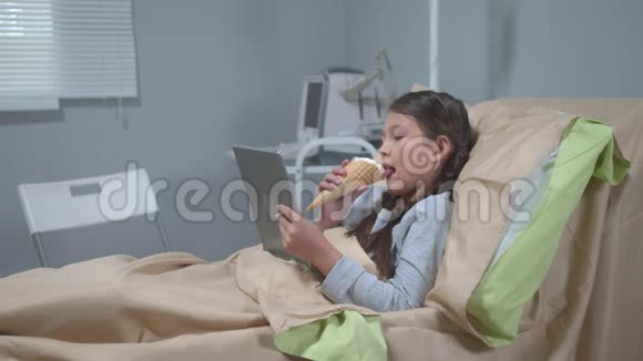 女孩躺在床上吃冰淇淋看平板电脑上的东西视频的预览图
