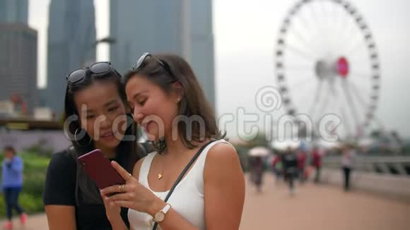 两个年轻的女人在阴天用大摩天轮看电话视频的预览图
