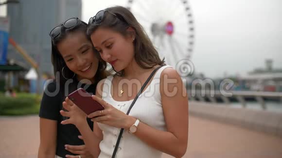 两个年轻的女人在电话里看着有趣的事情在大摩天轮上大笑视频的预览图