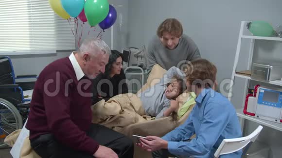 慢动作亲戚探望躺在医院床上的女孩男孩给大家展示照片视频的预览图
