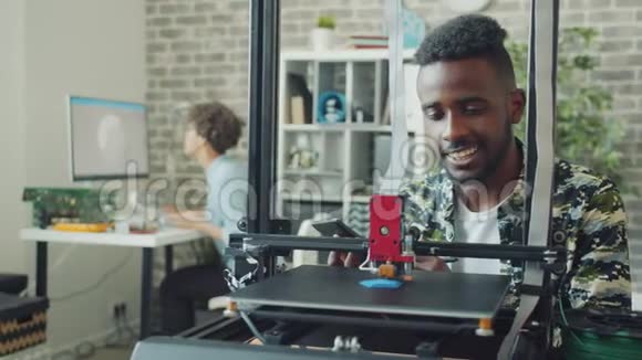 使用平板电脑的非裔美国人在办公室里看3d打印机制造模型视频的预览图