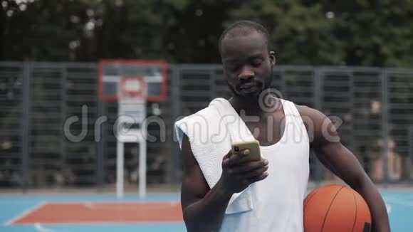 年轻的美国黑人一只手握着球一只手用智能手机视频的预览图