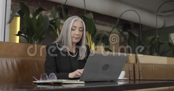 50多岁的时髦女人在笔记本电脑键盘上输入电子邮件微笑着可爱的女商人坐着视频的预览图