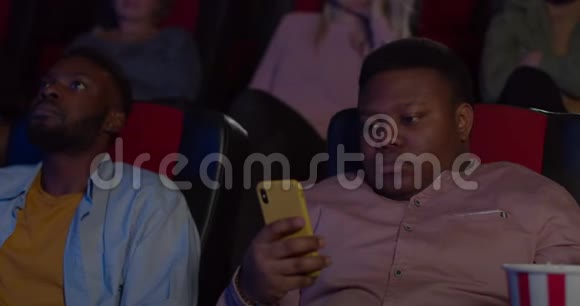 在使用智能手机的时候他的脸上露出惊讶的表情坐在电影院看电影的年轻人视频的预览图