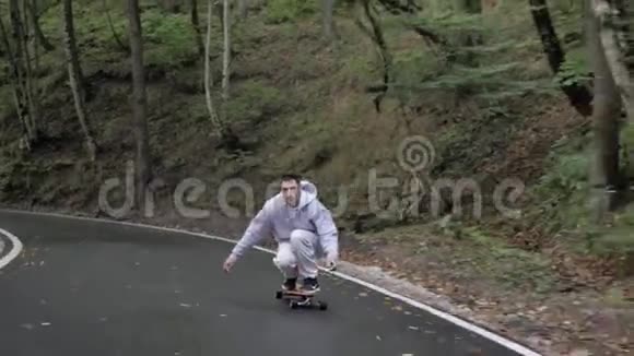 骑着灰色带帽的溜冰者坐着在蜿蜒的山路上乘坐游轮穿过山林近距离男子骑在滑板上视频的预览图