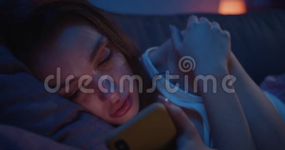 在智能手机上阅读旧信息时一个年轻沮丧的女孩在哭泣可怜的女人躺在沙发上视频的预览图