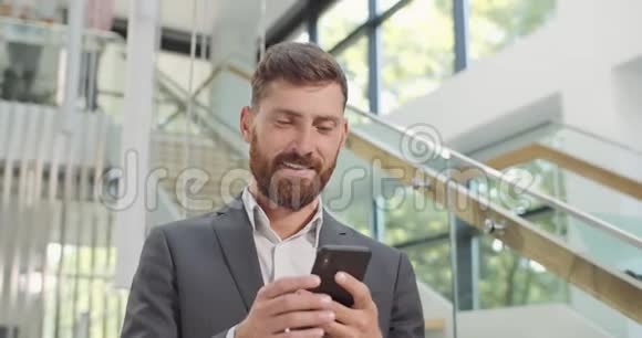 使用智能手机和站在现代办公室的胡子商人男性公司首席冲浪网视频的预览图