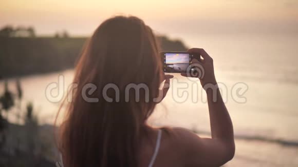 近距离观看年轻女子拍摄美丽海洋日落的照片和视频漂亮的女性拍照视频的预览图