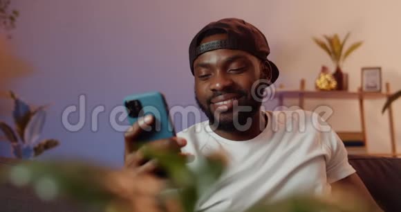 微笑的年轻人在使用智能手机时收到有趣的信息戴着黑色帽子的帅哥看着手机屏幕视频的预览图