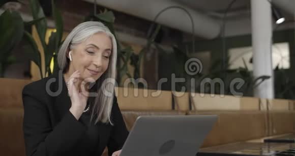 在笔记本电脑上举行视频会议的现代穿着正式西装的幸福老太太的侧面视图成熟优雅的女商人视频的预览图
