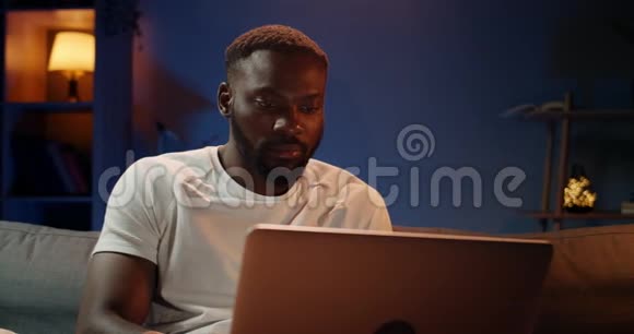 一个严肃的年轻人用他的笔记本电脑在家学习英俊的非洲学生打字视频的预览图