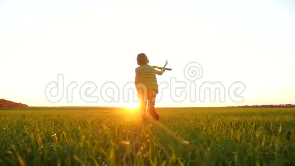 一个快乐的小男孩跑过一片绿色的草地玩着玩具飞机想象着飞行视频的预览图
