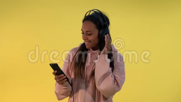 快乐的多民族女性用黄色背景耳机听音乐视频的预览图