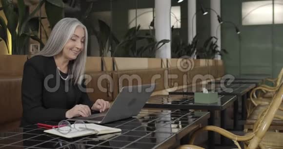 在咖啡馆里坐在沙发上使用笔记本电脑的成熟女商人的侧面视图美丽的中年妇女视频的预览图