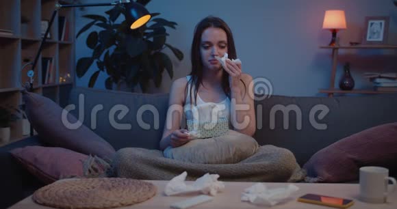 正面看年轻心烦意乱的女孩坐在沙发上用纸纸巾和吹鼻子沮丧的千年妇女视频的预览图