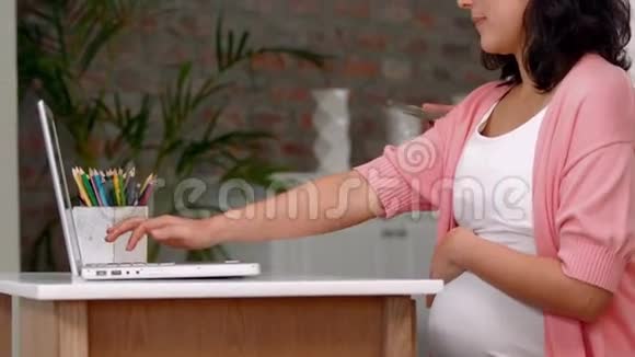 一位亚裔男子向怀孕的妻子展示数字平板电脑视频的预览图