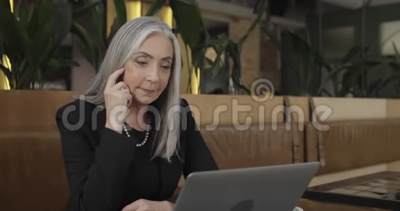 50多岁的成功女商人坐着看着笔记本电脑屏幕正式的漂亮老太太的正面景色视频的预览图