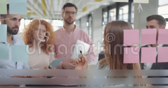 年轻的女队长用粘稠的音符在玻璃板上展示她的解决问题的技巧各办公室小组视频的预览图