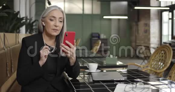 成熟女性企业家在耳足有视频电话智能手机与商业伙伴的正面看法中老年人视频的预览图