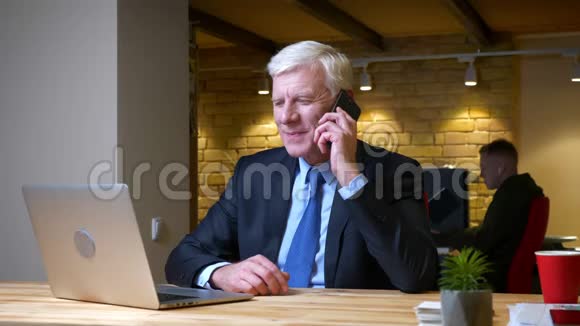 一个老白种人商人用笔记本电脑在电话上愉快地笑着交谈的特写镜头视频的预览图