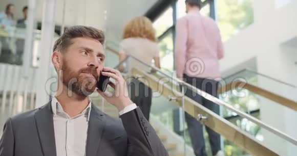 一群英俊的商人在他的智能手机上交谈站在办公楼里男性办公室职员视频的预览图
