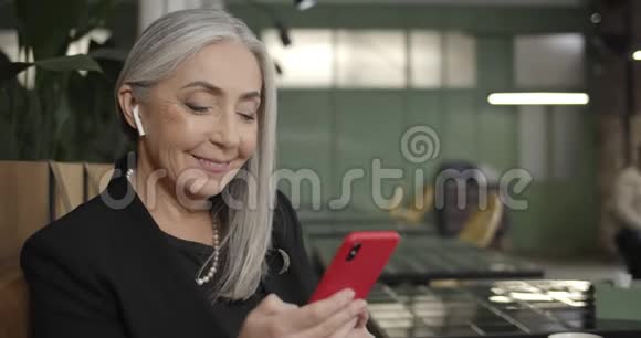 用智能手机和打字用耳脚关闭老女企业主现代成熟的女人坐在咖啡馆里视频的预览图