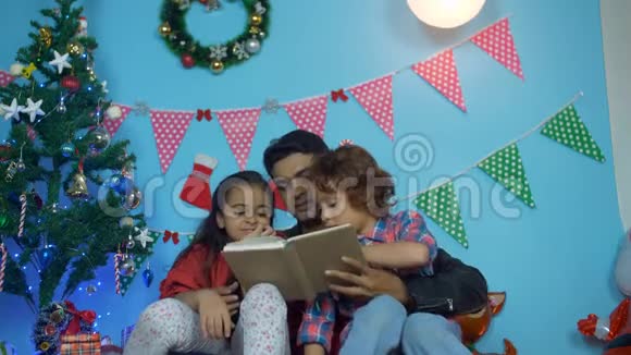快乐的印度父亲在圣诞假期给他可爱的孩子们读故事书视频的预览图