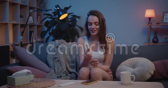 幸福的女孩坐在沙发上拿着一个积极的怀孕测试年轻女子对积极的结果感到兴奋视频的预览图
