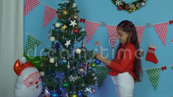 快乐的小女孩在圣诞树上挂着五颜六色的球和其他美丽的物品节日的场景视频的预览图