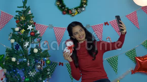 在圣诞节期间一个漂亮的印度女孩和一个小堆玩具雪人打着自拍视频的预览图