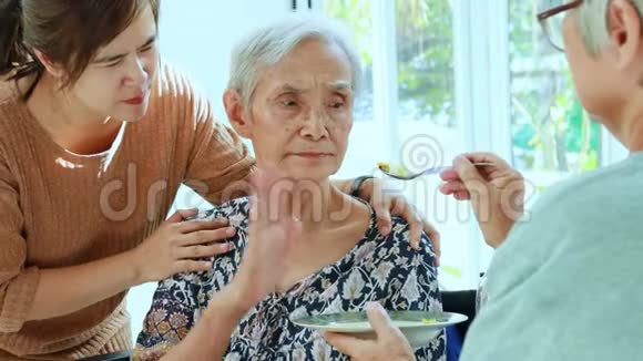 亚洲的女儿老年妇女或家庭朋友在轮椅上喂养老年病人或母亲劳累厌倦食物少吃食物视频的预览图