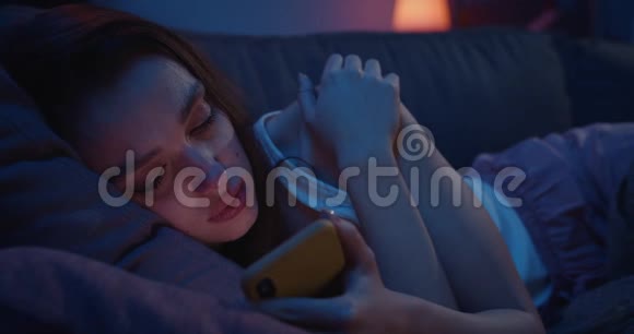 一个孤独的年轻女子躺在沙发上晚上使用智能手机一位沮丧的千禧女性视频的预览图