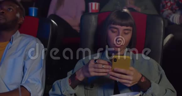 在电影院里围着一个无聊的时髦女孩坐着吃爆米花千禧年的女人视频的预览图