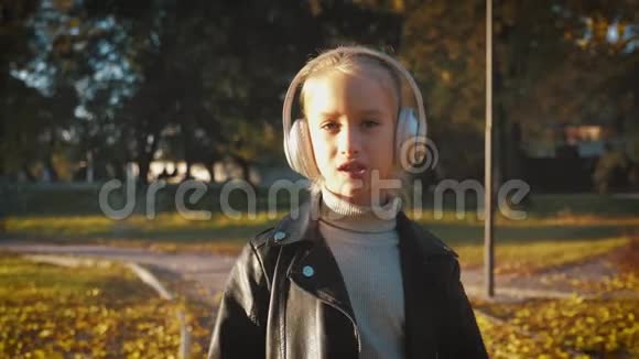 阳光明媚的一天带着耳机的年轻女孩在户外年轻时髦漂亮的孩子听音乐耳机视频的预览图