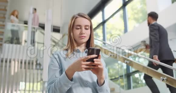 年轻有魅力的女上班族使用智能手机站在楼梯附近女商人给她打字视频的预览图