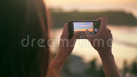 近距离观看年轻女子制作美丽的海上日落照片和视频漂亮的女性拍照视频的预览图