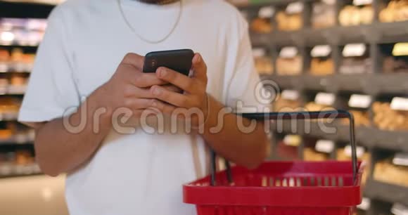 从作物的角度来看男人使用他的现代手机同时站在购物篮他发短信聊天视频的预览图