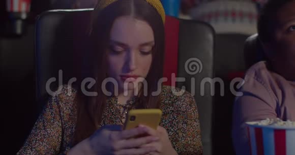 在使用智能手机时一个漂亮的女孩做着惊讶的表情坐在电影院的年轻美女视频的预览图