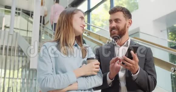 年轻的女人和英俊的男同事说话笑微笑男女办公室职员站在大厅和视频的预览图
