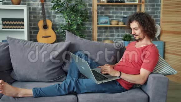 在家工作的男性自由职业者坐在沙发上微笑着打字视频的预览图