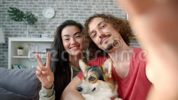 一对幸福的夫妇在家里和科吉狗自拍竖起大拇指的照片视频的预览图